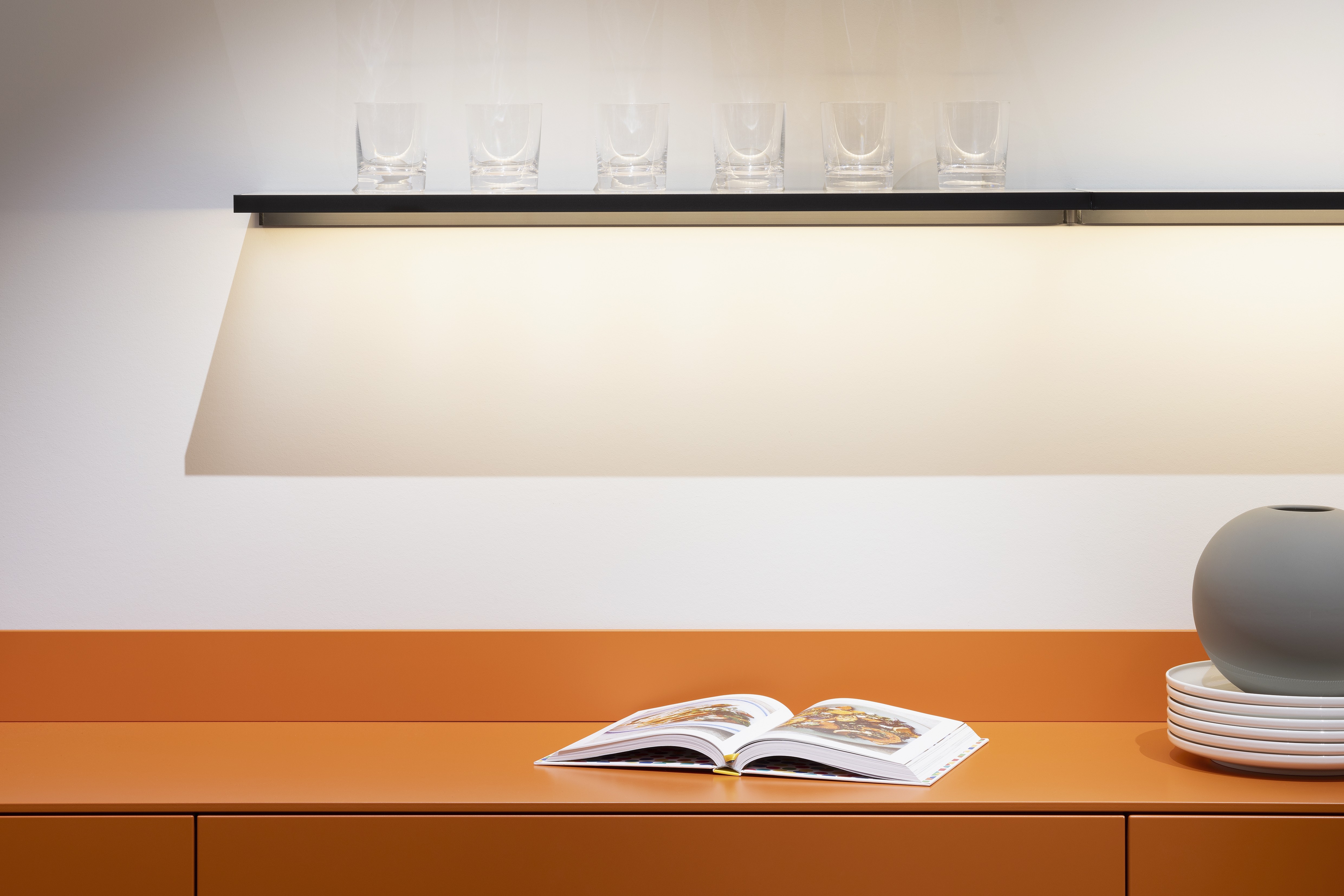 APL: 171 Greige 16 mm Front: AV 7010-GL Beton-grau, mineralischer Spachtelbeton (PUResist, PURemmision) Front Lack Orange Korpus: 2059 Designkorpus Titan Griff: Metall Black Chrome und Kehlleiste 359 Greige matt Kehlleiste Graphit gebürstet Geräte: Gaggenau Armatur: Franke Spüle: Franke  Features: Betonoberfläche individuell nachbearbeitet, Nischenrückwand Regal Betonoberfläche, Sideboard Orange mit offenen Schubkästen in Plexiglas Orange exklusives Auszugssystem im Schrank für mehr Stauraum, Sideboard 