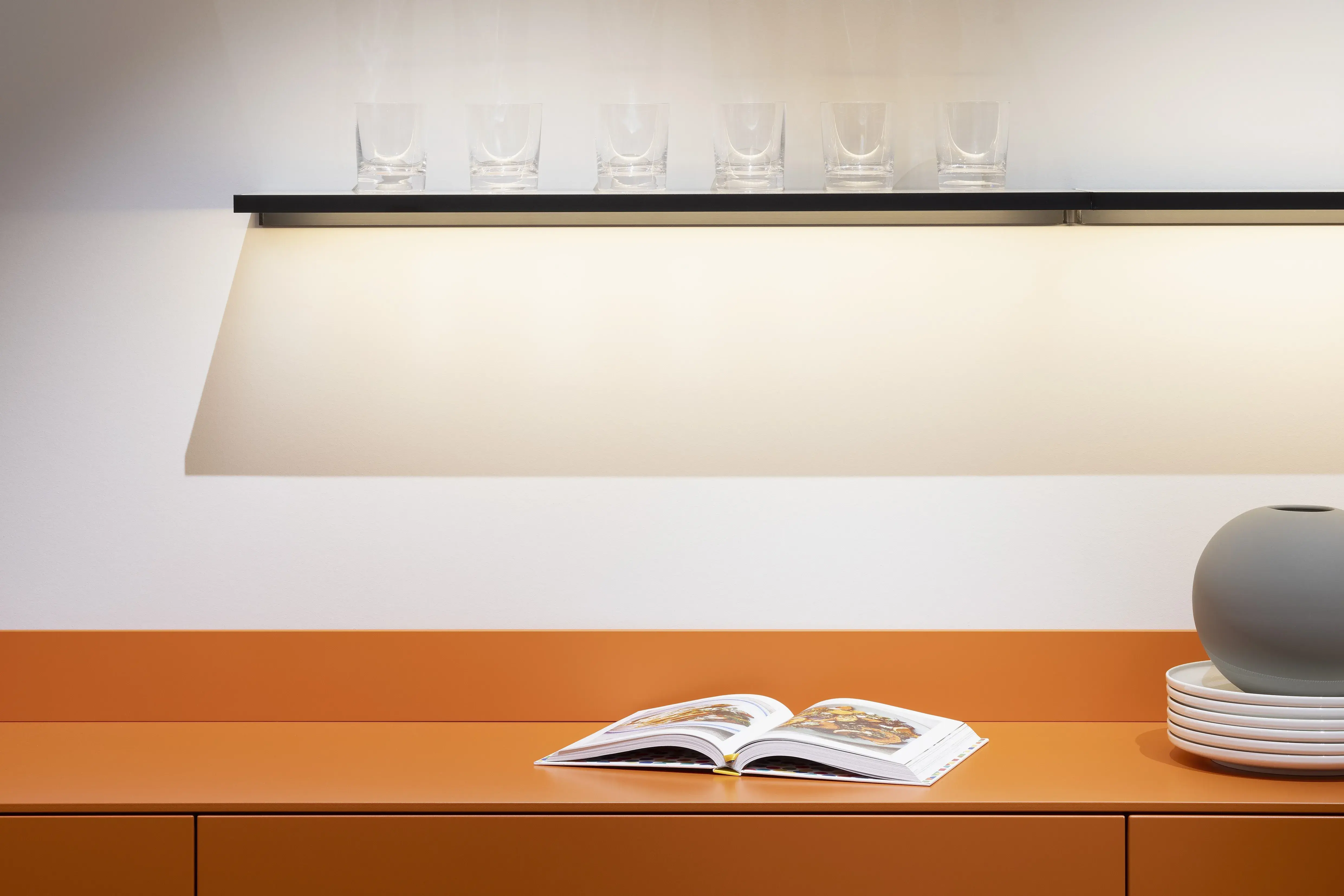 APL: 171 Greige 16 mm Front: AV 7010-GL Beton-grau, mineralischer Spachtelbeton (PUResist, PURemmision) Front Lack Orange Korpus: 2059 Designkorpus Titan Griff: Metall Black Chrome und Kehlleiste 359 Greige matt Kehlleiste Graphit gebürstet Geräte: Gaggenau Armatur: Franke Spüle: Franke  Features: Betonoberfläche individuell nachbearbeitet, Nischenrückwand Regal Betonoberfläche, Sideboard Orange mit offenen Schubkästen in Plexiglas Orange exklusives Auszugssystem im Schrank für mehr Stauraum, Sideboard 