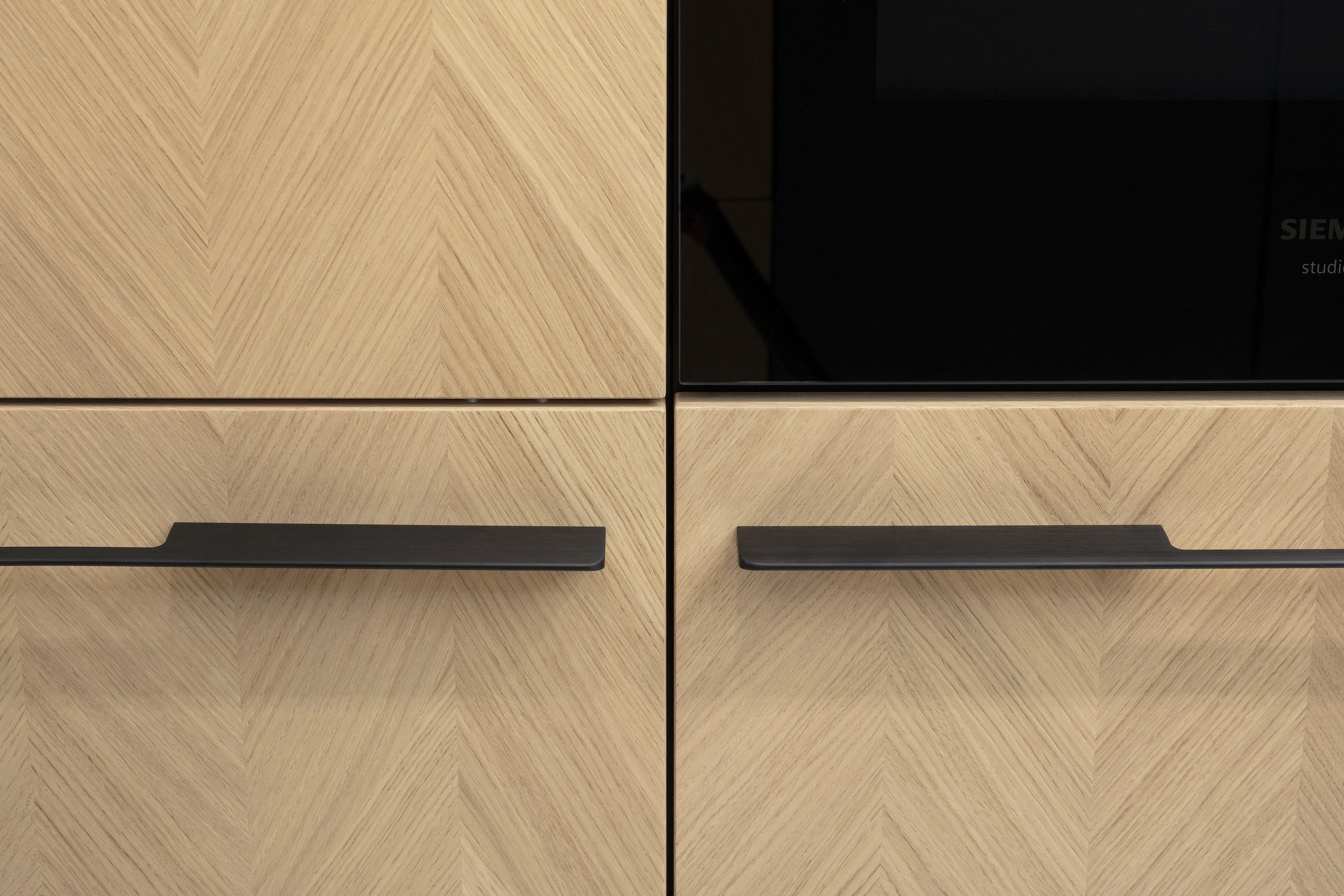 Front: Intarsia Gavi Eiche Furnier Resopal Brown Powder supermatt Korpus Schwarz APL: Resopal Brown Powder supermatt Geräte: Siemens Studio Line Spüle und Armatur: Blanco   Features: Front Echtholz Fischgrät-Optik, Kombination Echtholz und Resopal supermatt, Einbautür in Frontmaterial Resopal, Küchentheke Massivholz, APL = Korpusfarbe = Frontmaterial, Kombination Griffleiste und grifflos, Korpus in Frontmaterial, Wärmeschublade, Spüle und Armatur Schwarz, Besteckeinsatz. 